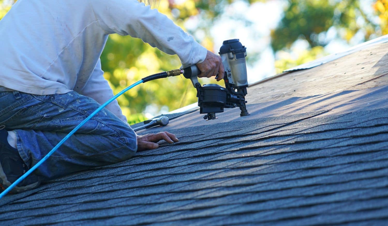 man using nail gun to put shingles on roof